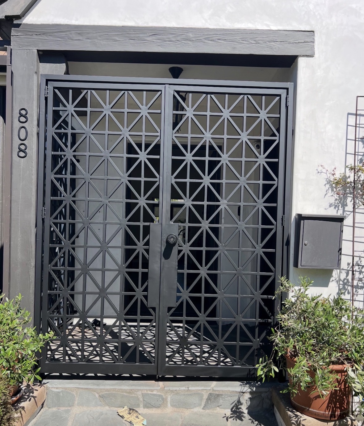 Black laser-cut double entry gate on a white stucco home