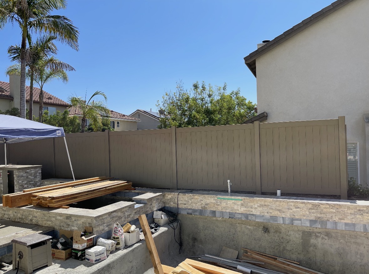 Long tan vinyl privacy fence behind a backyard